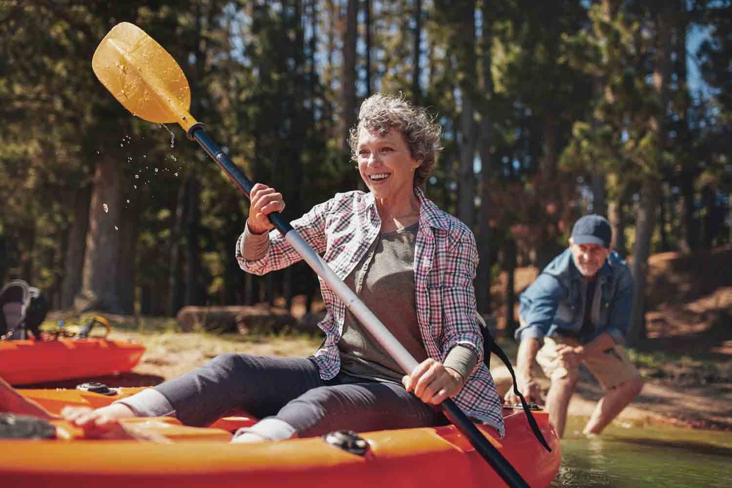 Lady smiling and holding a paddle on a canoe under the sun.