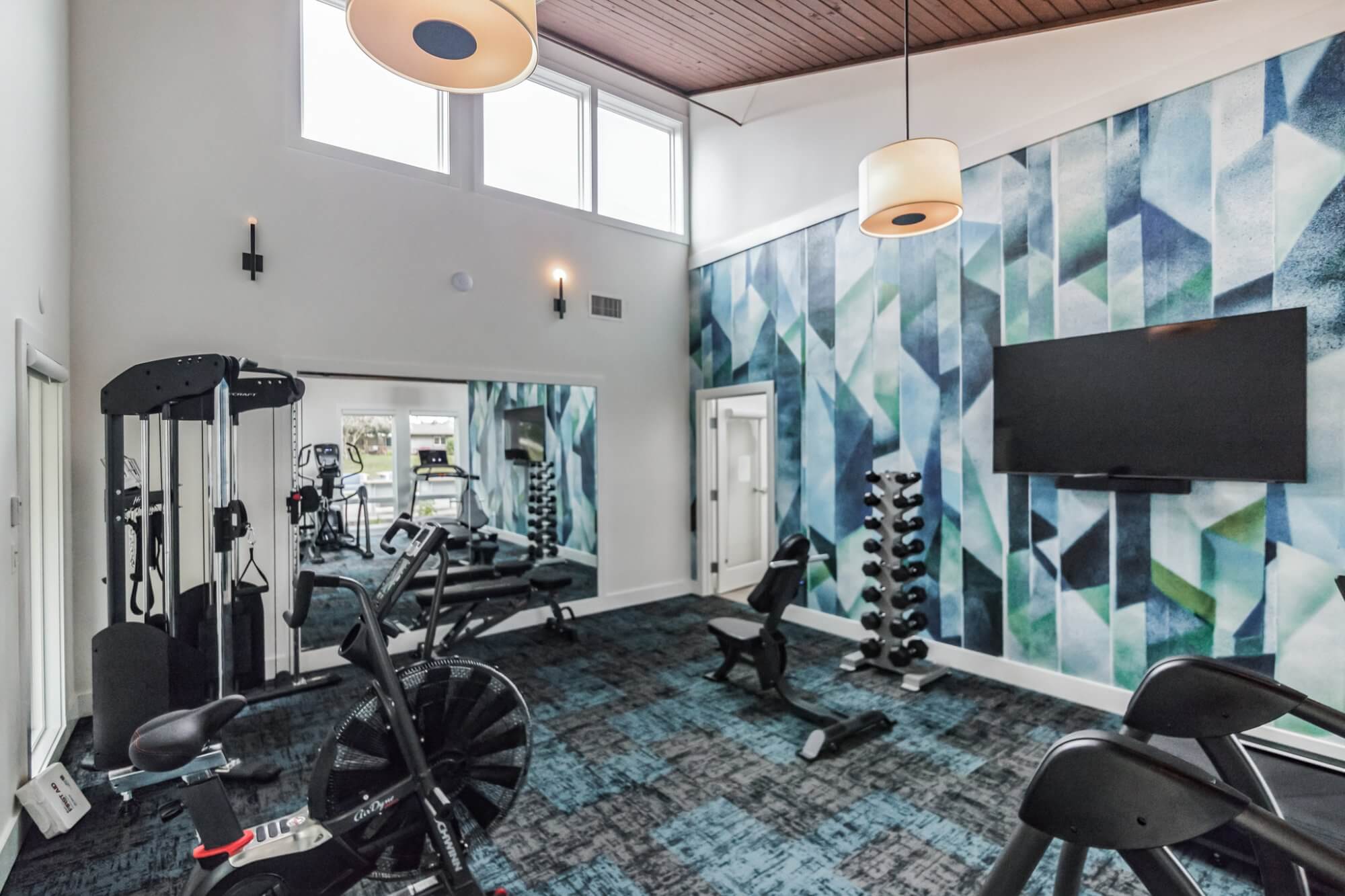 Modern fitness room with exercise equipment, a large mirror, and a geometric blue and green wall design in Olympia